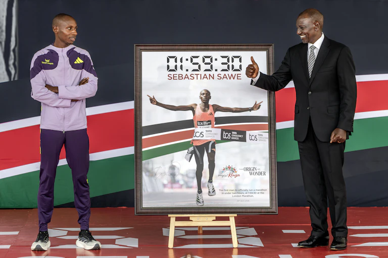 Photo en pied des deux hommes placés de part et d'autre d'un panneau affichant le temps obtenu par le coureur, 01:59:30.