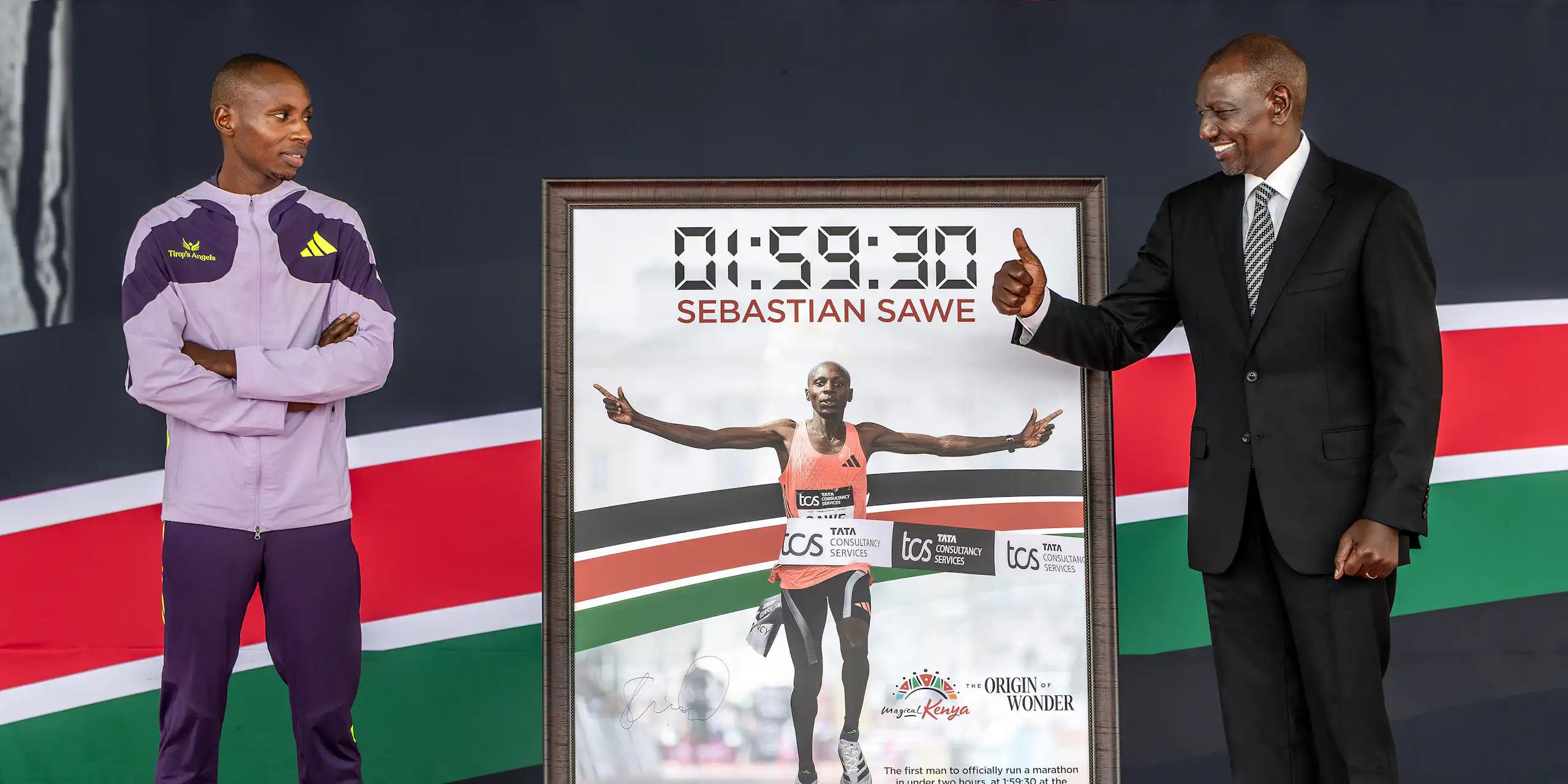 Photo en pied des deux hommes placés de part et d'autre d'un panneau affichant le temps obtenu par le coureur, 01:59:30.