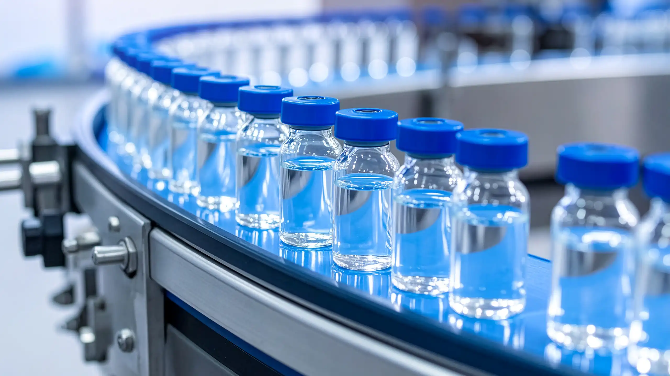 Pharmaceutical production line with rows of glass vaccine vials on conveyor belt.