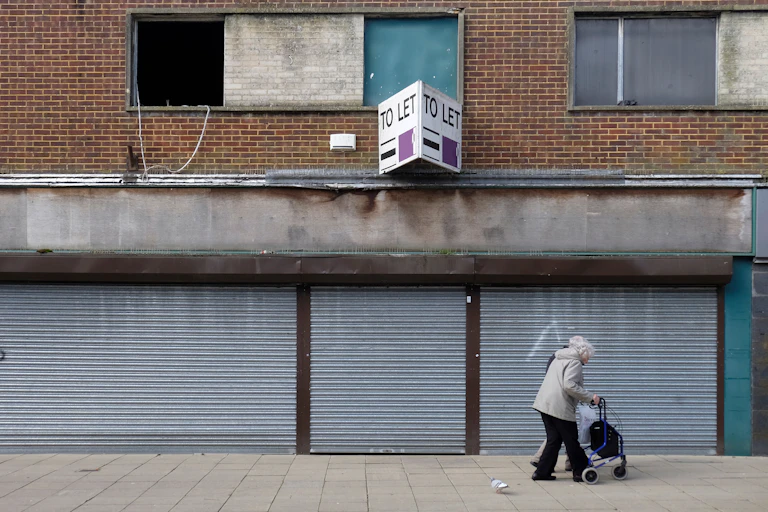 Elderly lady walking past boarded up shop