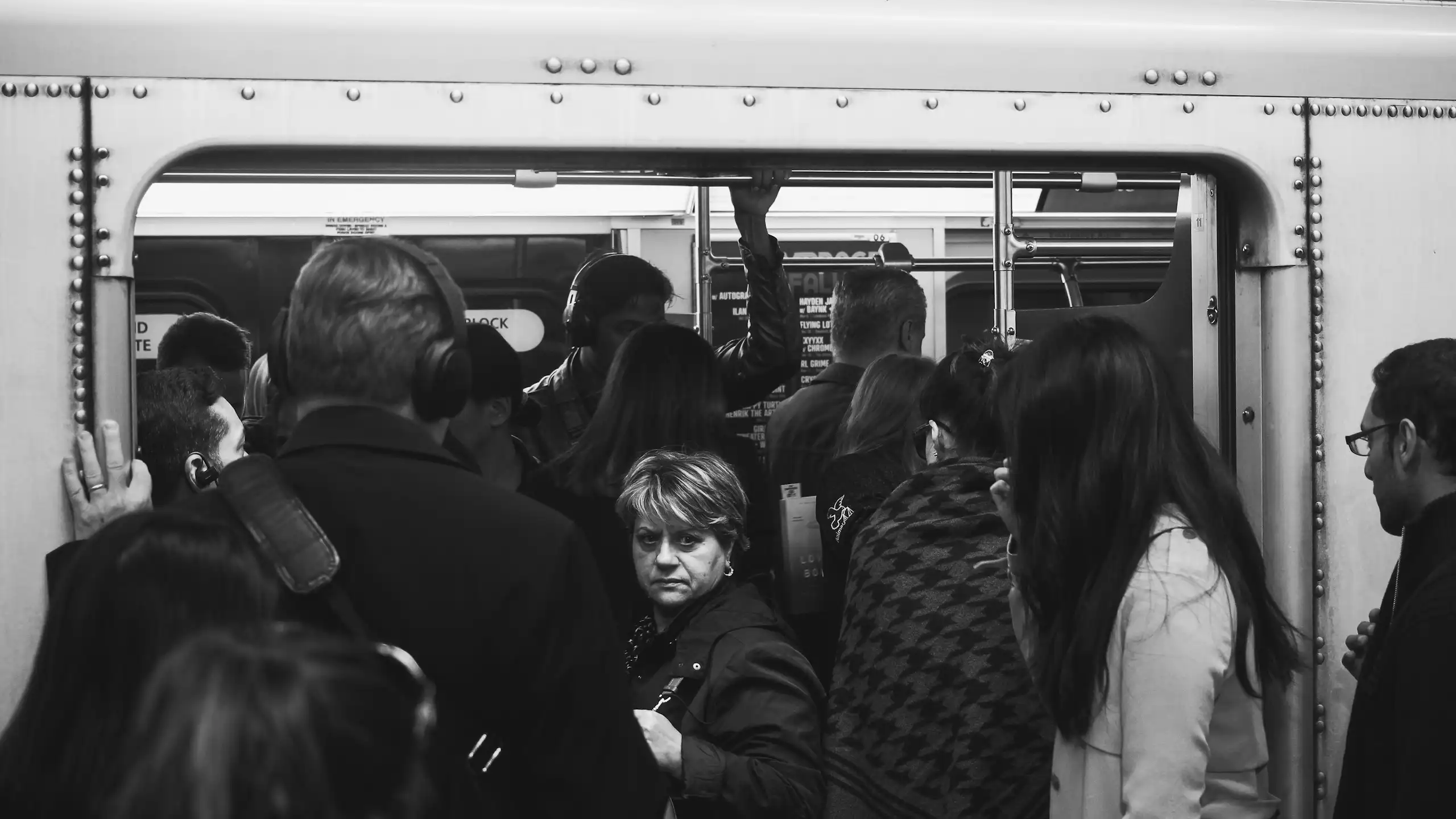 A group of people packed into a subway car with an older woman looking back.