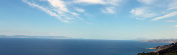 A photo of two land masses, one far in the distance, with ocean and sky between them.
