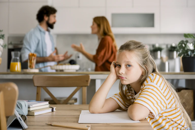 Displeased girl leans on table while man and woman have heated discussion in background