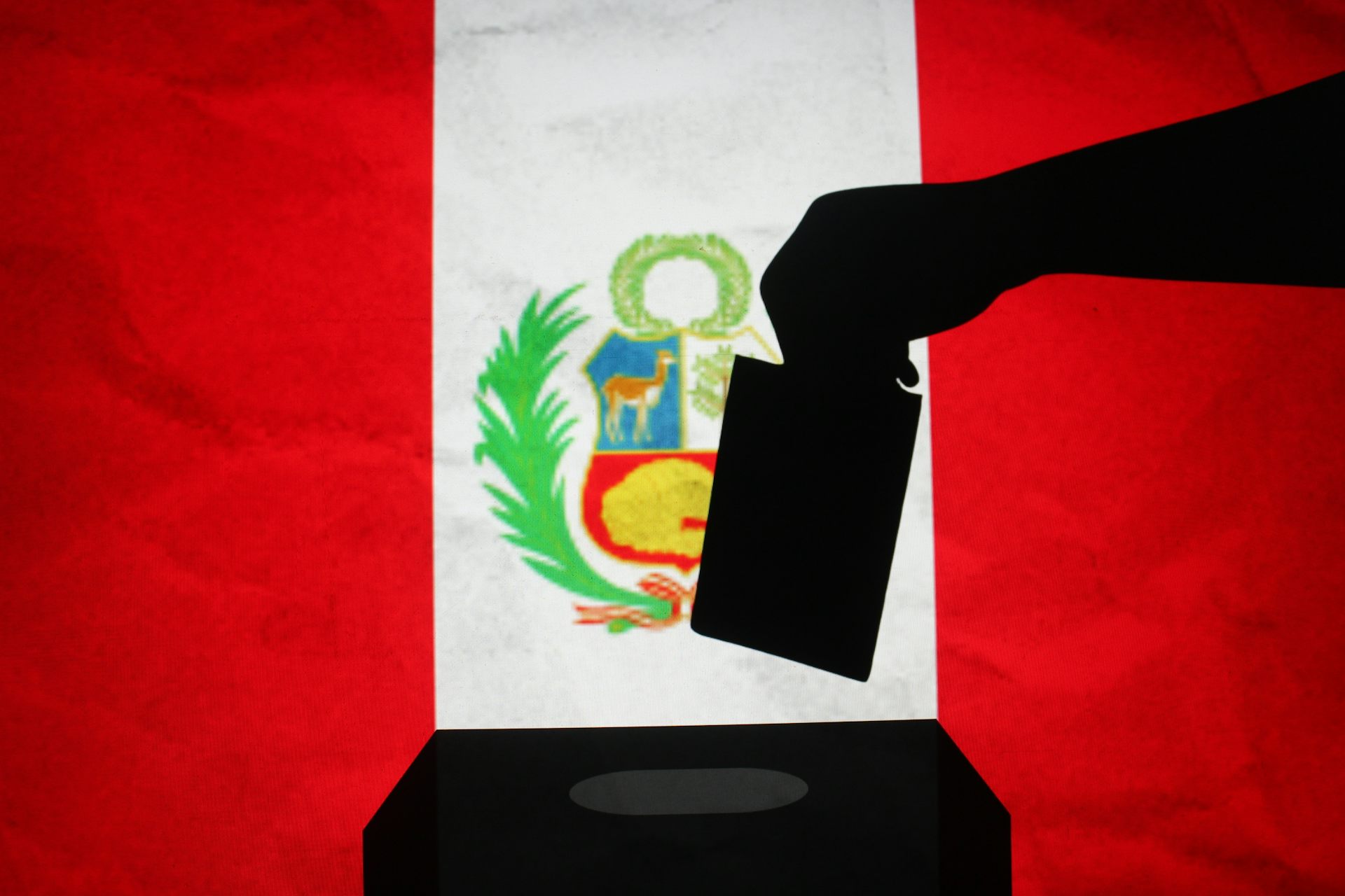 Silueta de una mano introduciendo un voto en una urna con la bandera de Perú al fondo