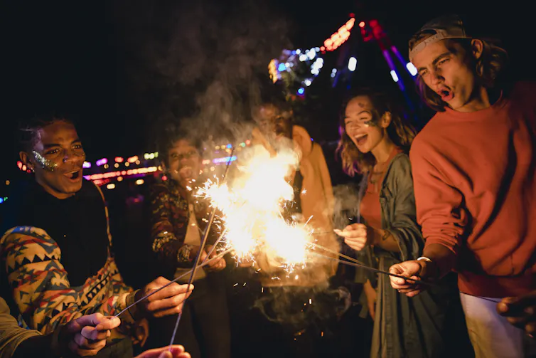 Small group of young adults standing in a circle holding sparklers in a festive setting.