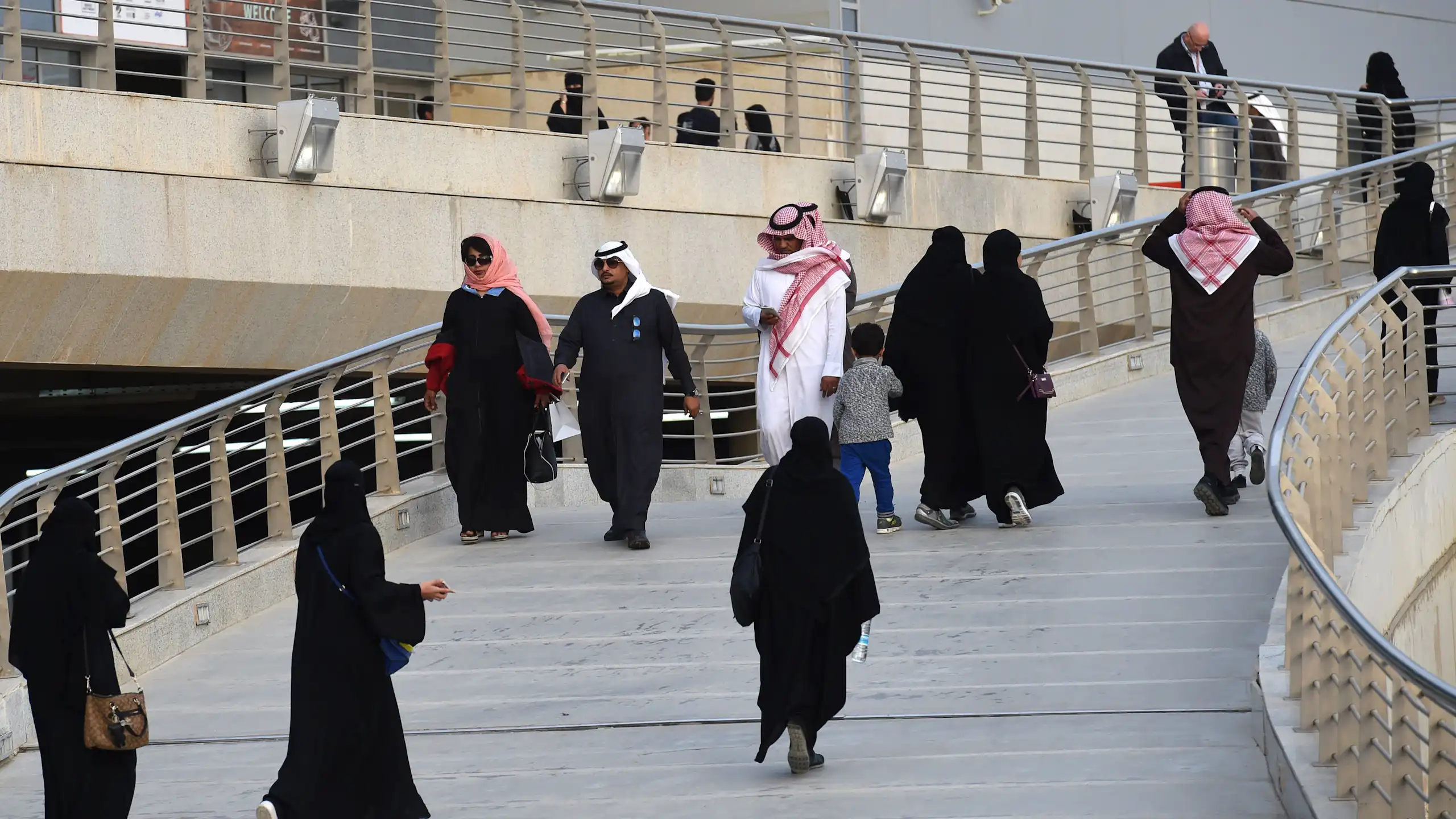 A group of people in traditional Saudi dress walk up stairs.