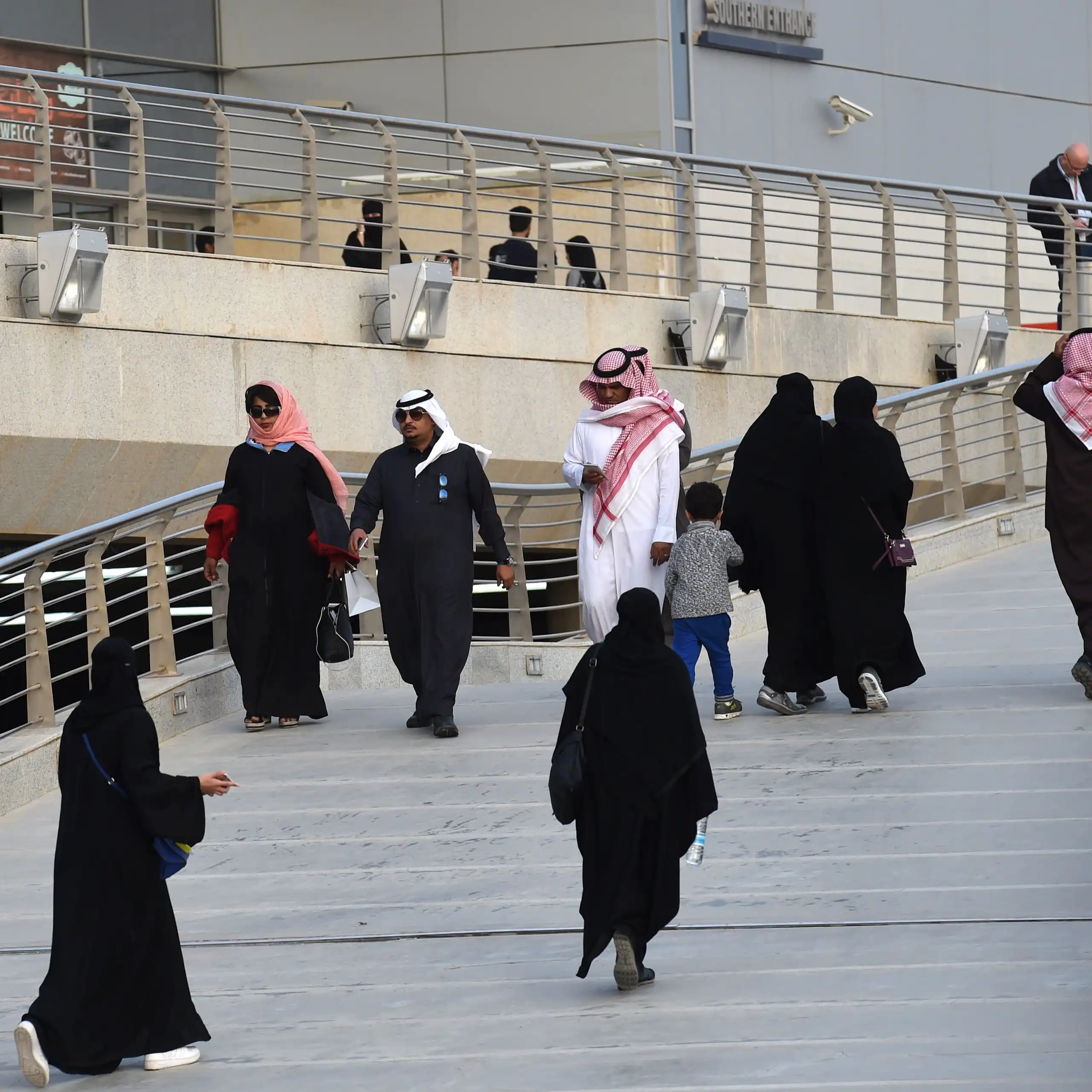 A group of people in traditional Saudi dress walk up stairs.