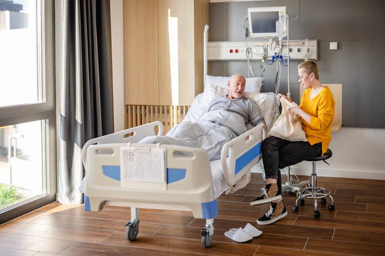 A man in hospital instructs his daughter, who is opening a bag