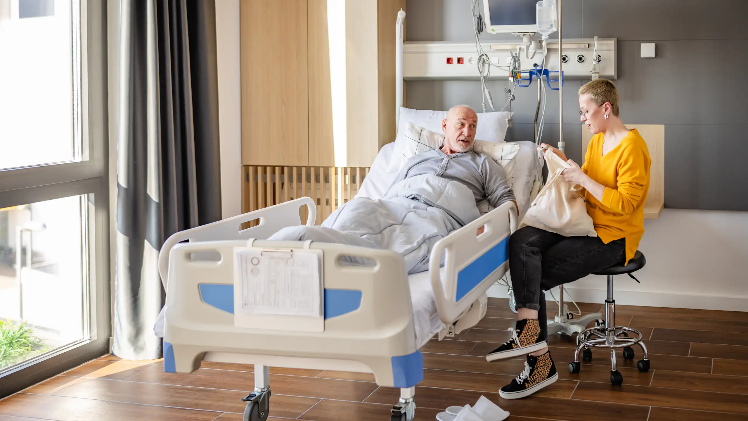A man in hospital instructs his daughter, who is opening a bag