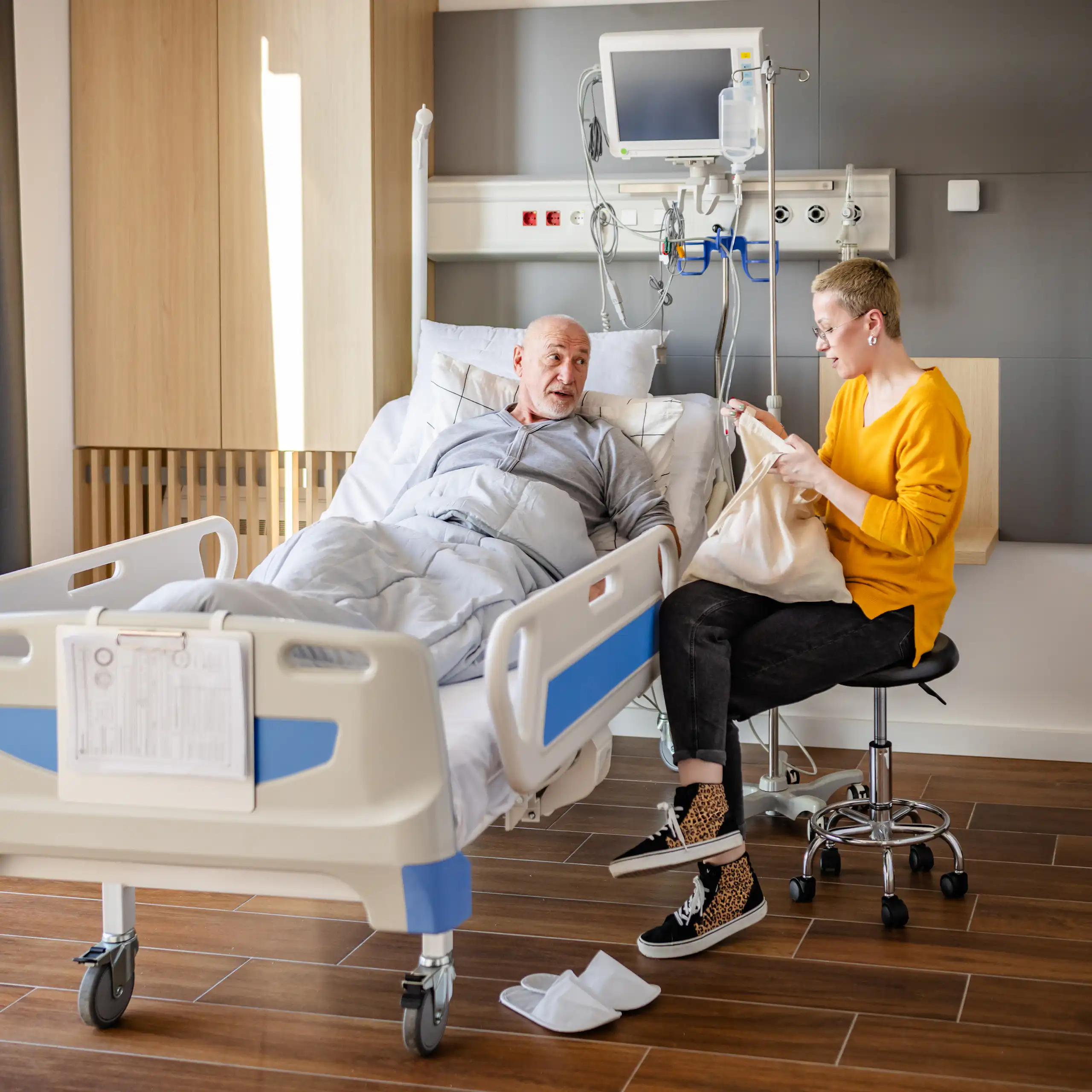 A man in hospital instructs his daughter, who is opening a bag