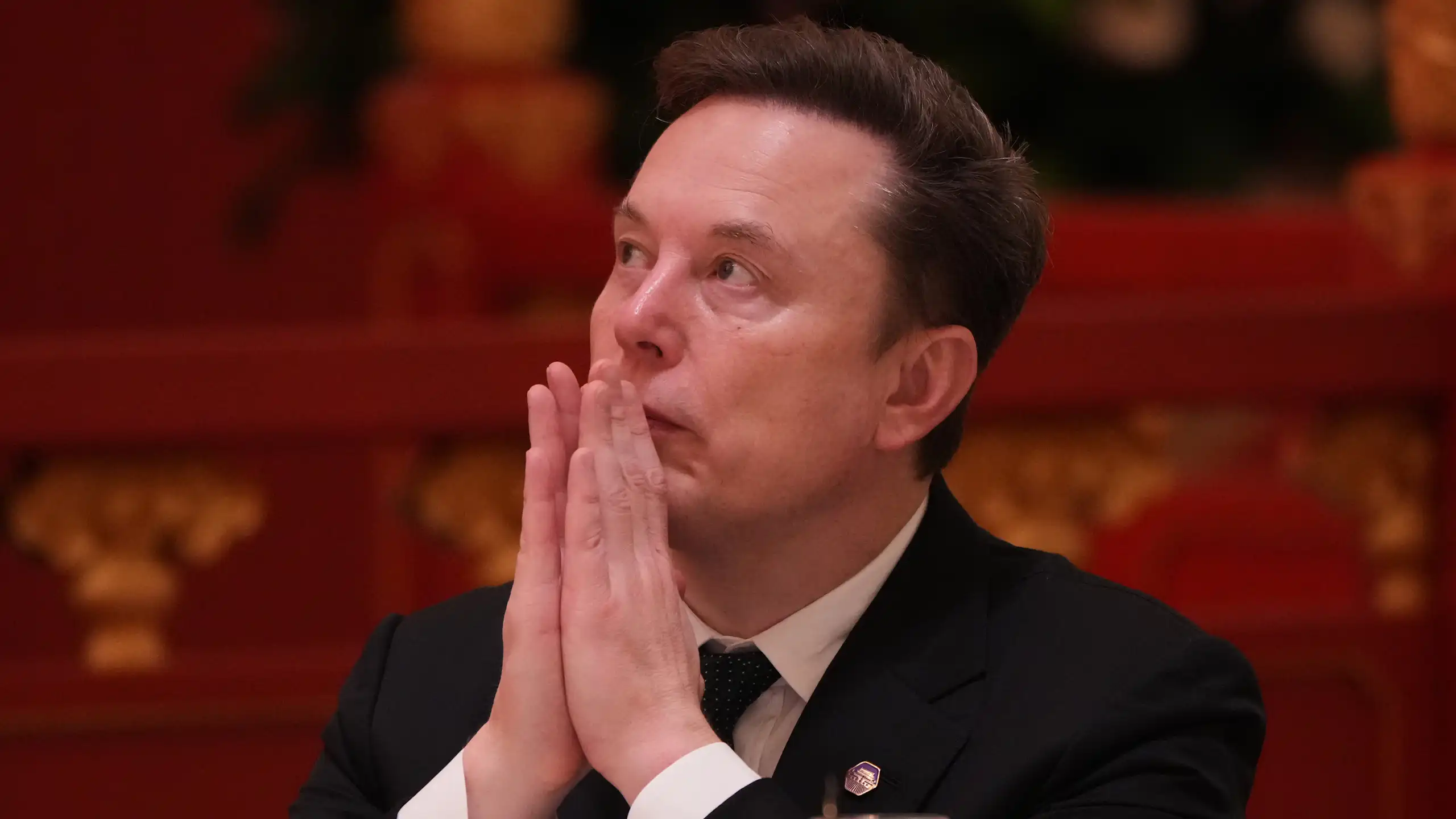 Elon Musk with his hands held up to his mouth