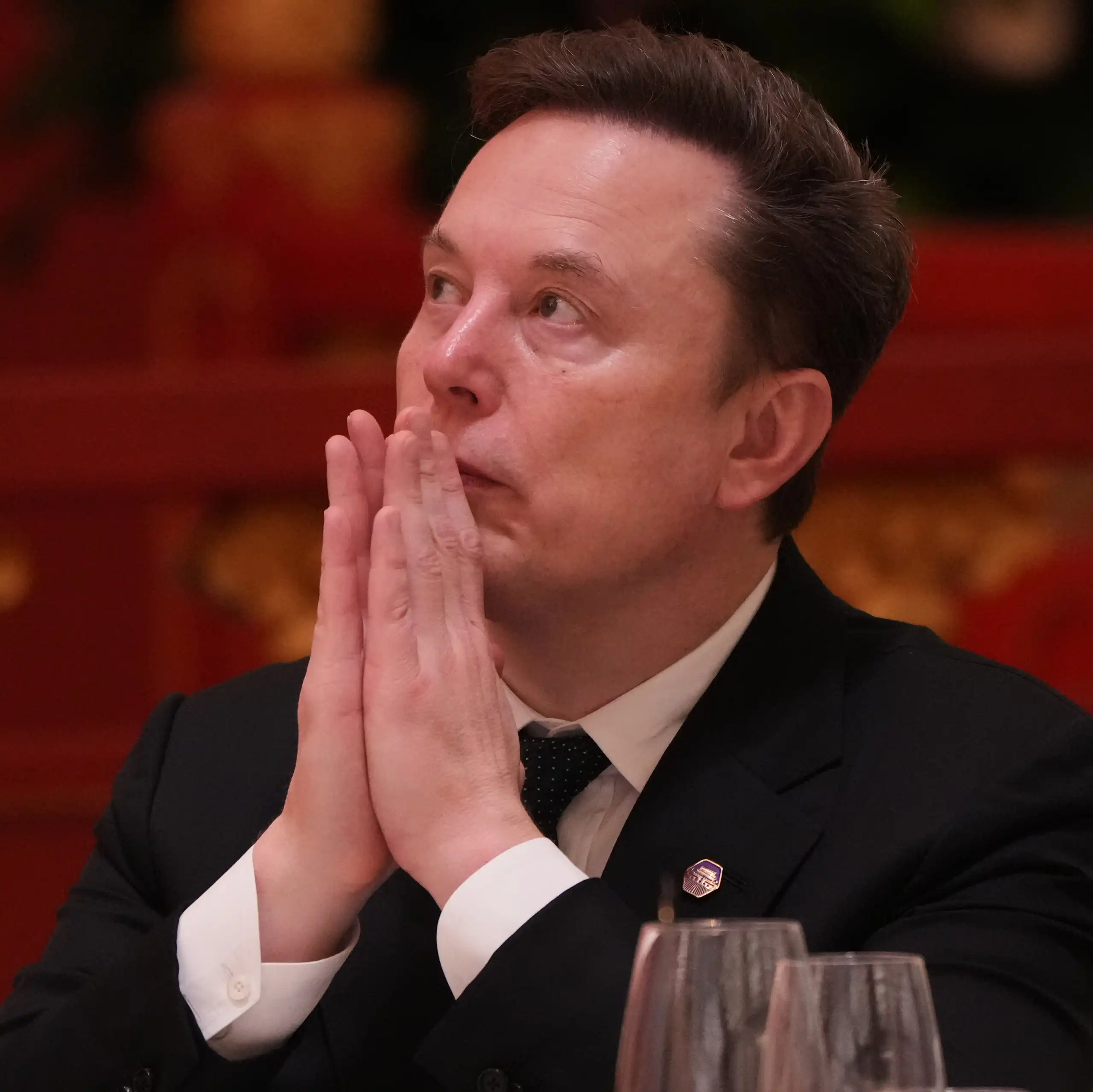 Elon Musk with his hands held up to his mouth