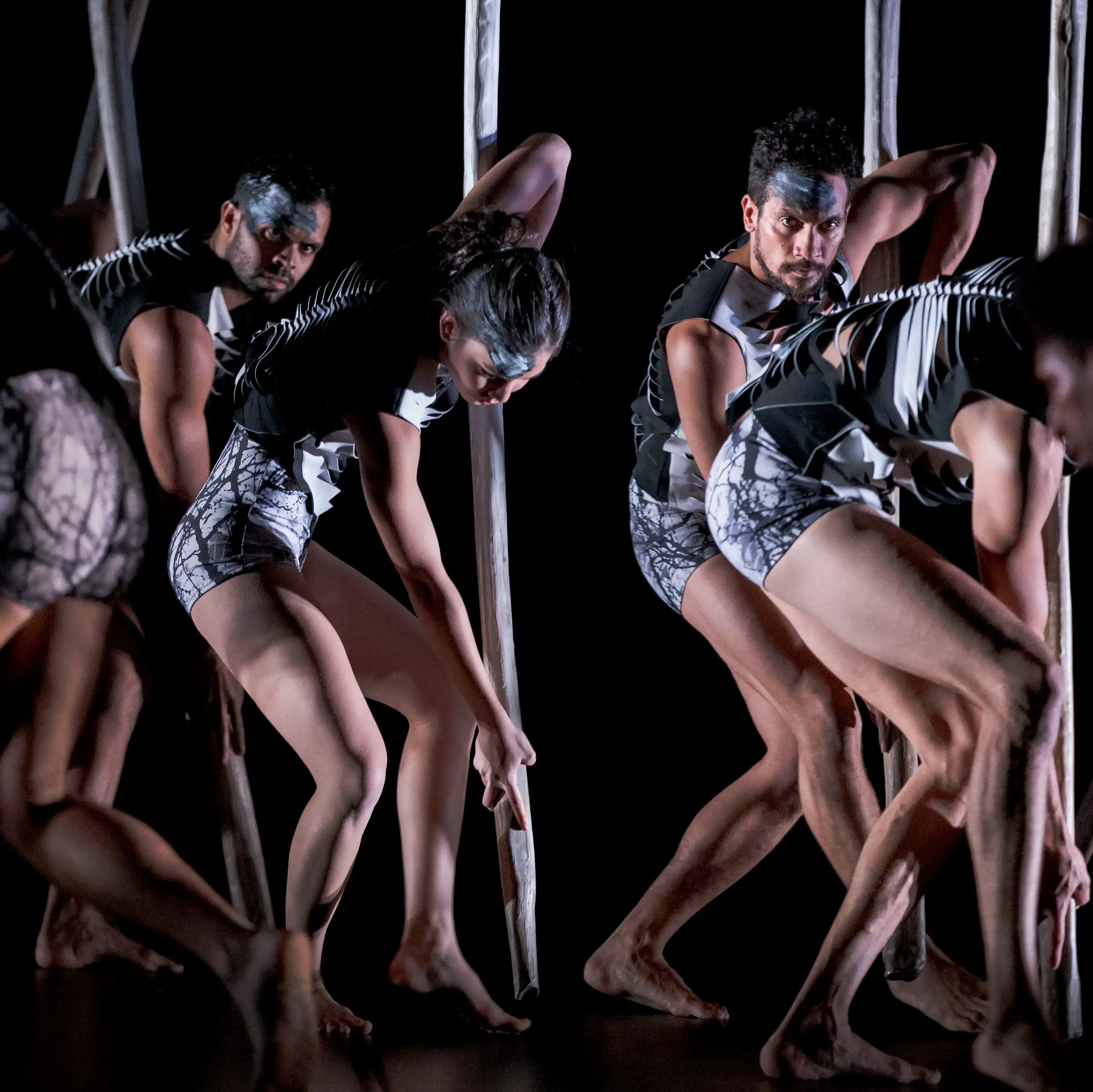 An ensemble of dancers in skeleton-like outfits march across a dark stage.