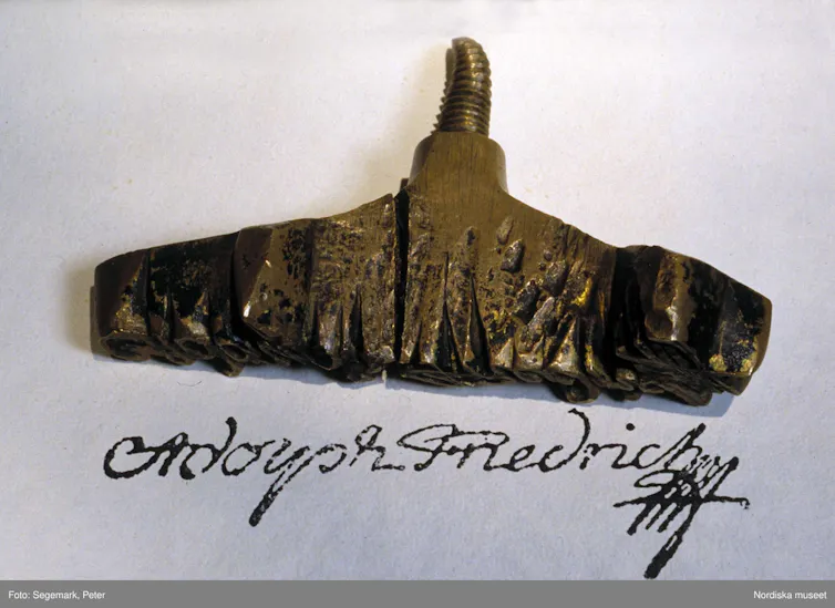 A metal signature stamp with a print of the signature on paper