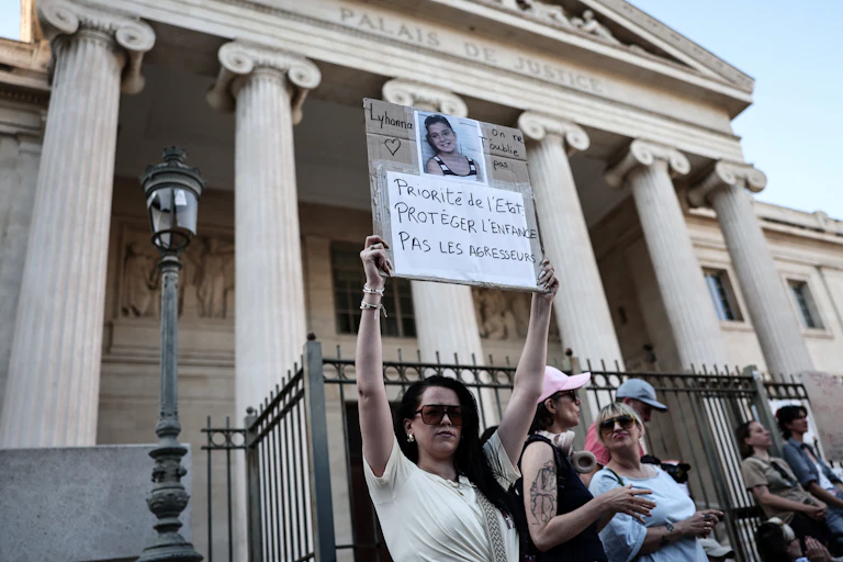 Une manifestante tient une pancarte et la photo de l’enfant devant le palais de justice de Marseille : « Lyhanna, on ne t’oublie pas. Priorité de l’État : protéger l’enfance, pas les agresseurs ! »