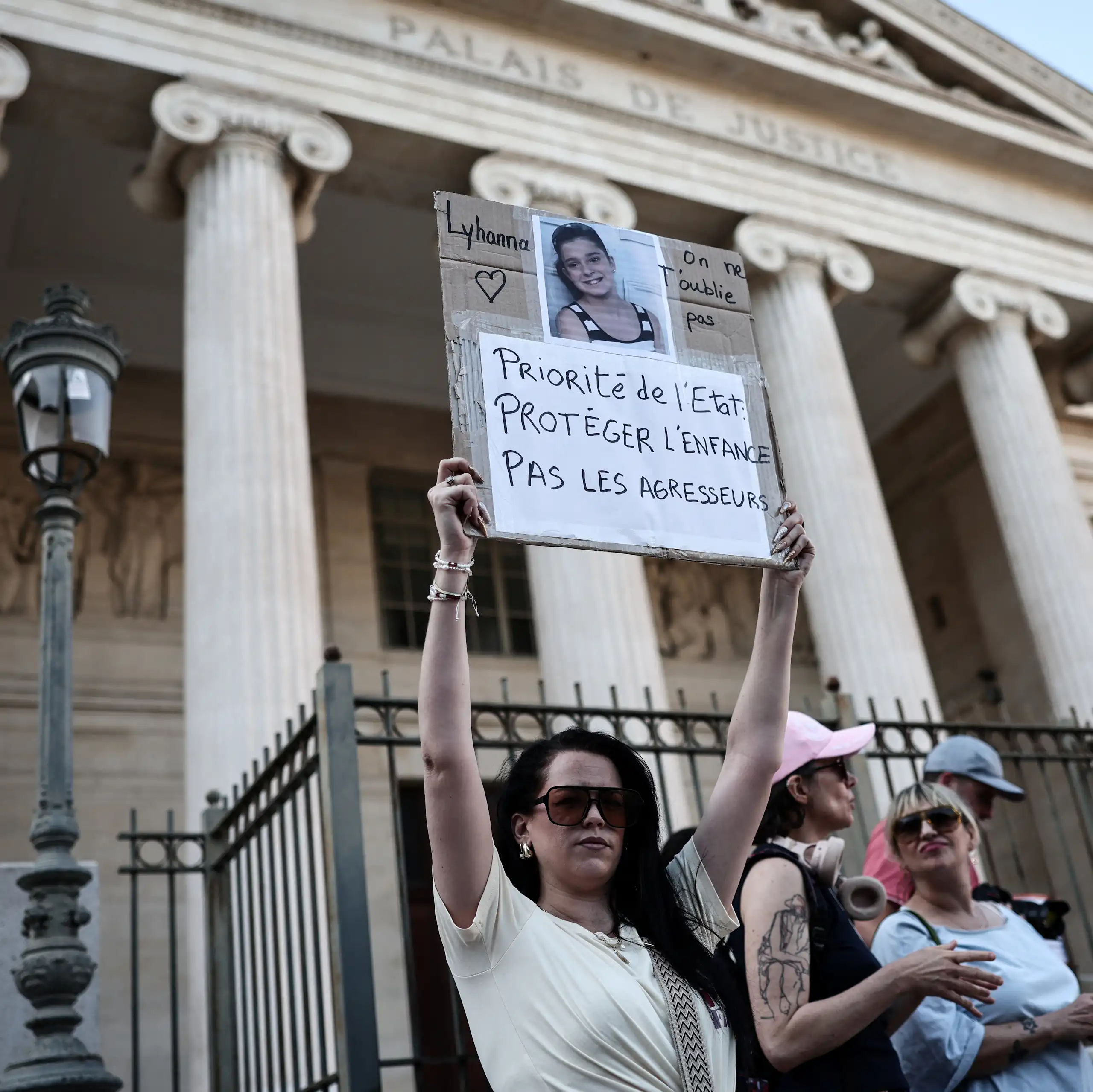 Une manifestante tient une pancarte et la photo de l’enfant devant le palais de justice de Marseille : « Lyhanna, on ne t’oublie pas. Priorité de l’État : protéger l’enfance, pas les agresseurs ! »