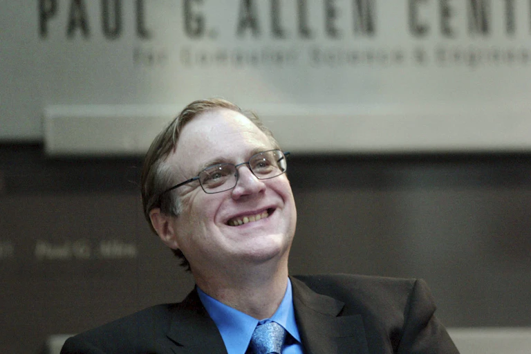 A man in a suit and tie smiles while looking upward against a backdrop that says 'Paul G. Allen Center.'