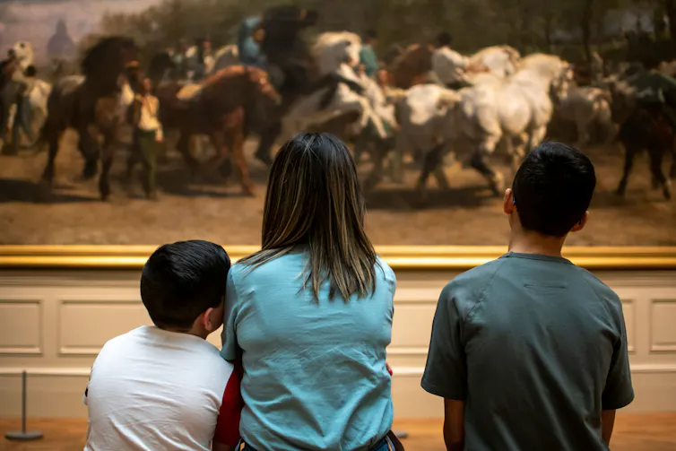 Un día en el museo: cómo seguir las pautas de los niños para apoyar la curiosidad intergeneracional 4 Personas vistas en un banco mirando la pintura.