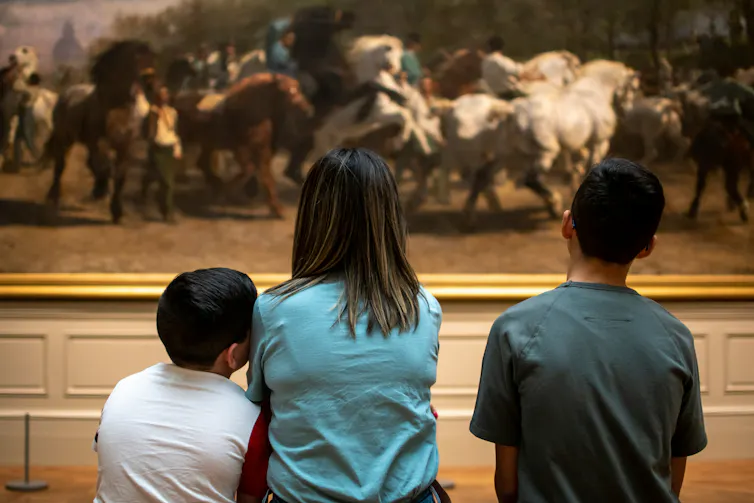 People seen on a bench looking at a painting.