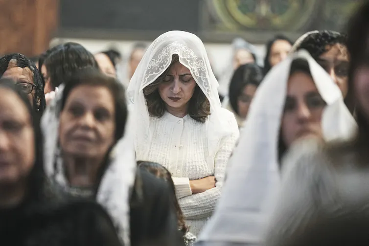 Women with white scarves draped over their heads stand in rows of pews.