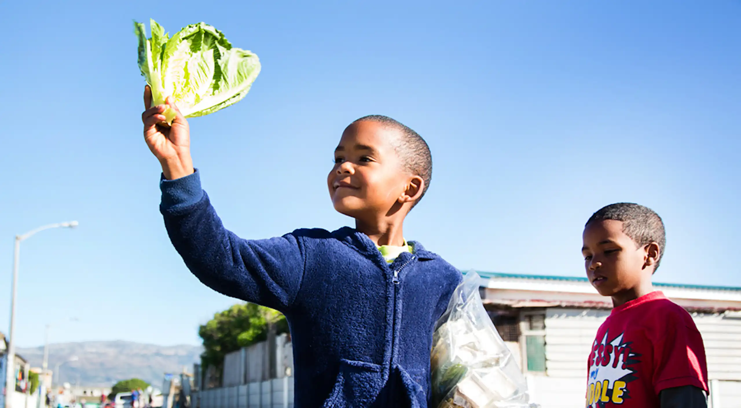A child stands smiling holding lettuce and bean sprouts