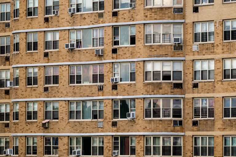 A view of a large brick building with windows, air conditioners and heating vents visible.