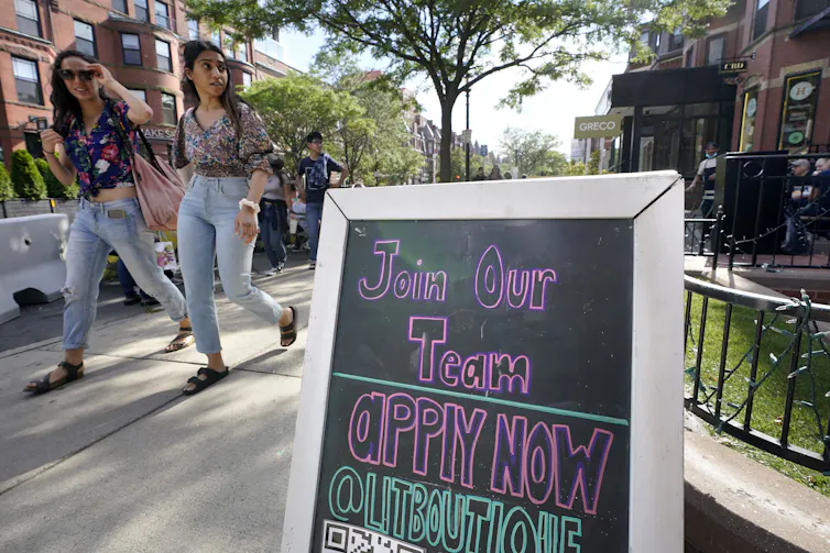 A hiring sign propped up on a sidewalk