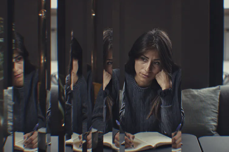 Todo el mundo quiere pensar que tiene la mente abierta: he aquí por qué la mayoría de la gente no lo es 1 Una morena escribe en un diario y parece pensativa, su rostro parcialmente reflejado en varios finos paneles de vidrio.