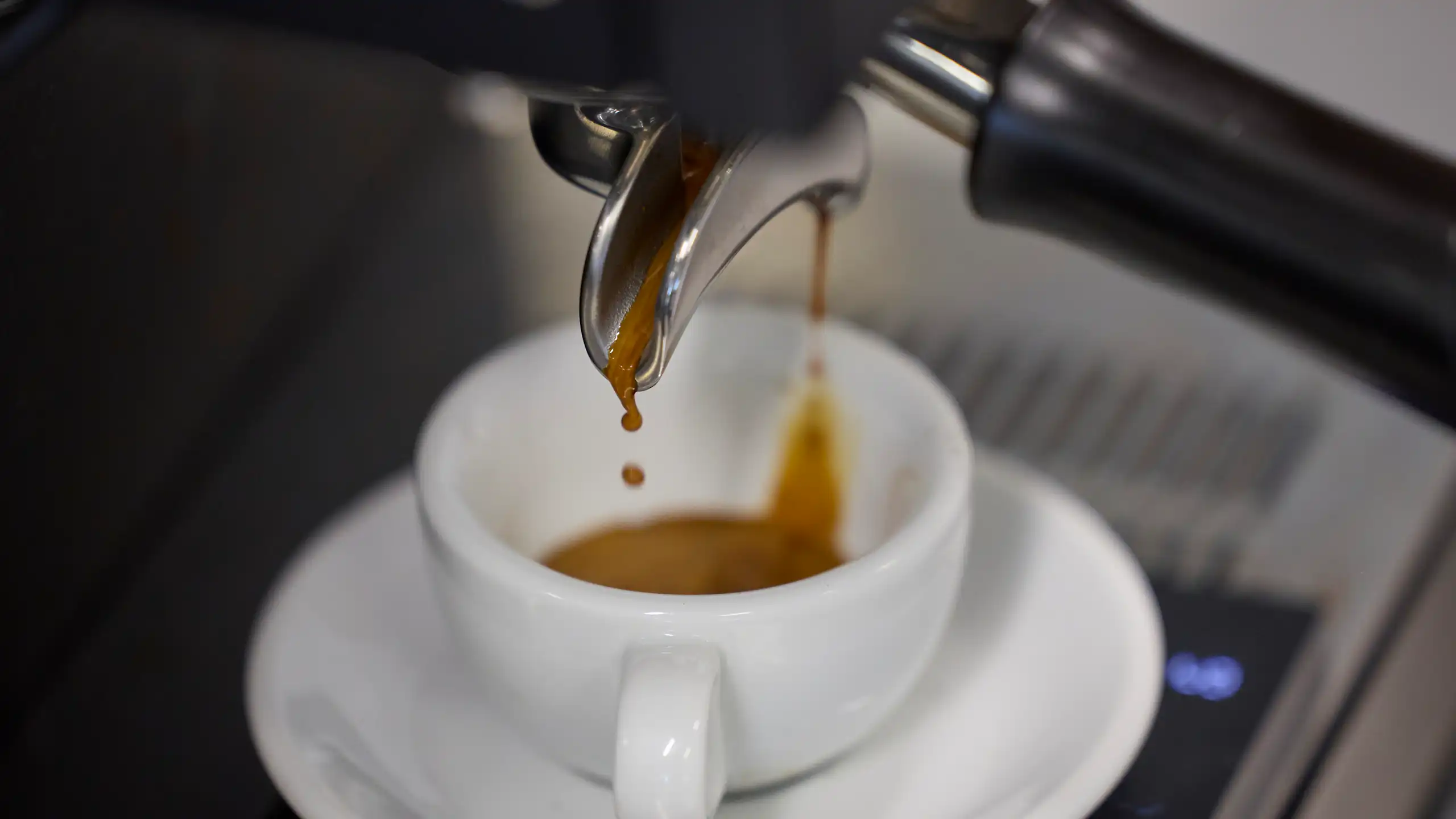 Espresso dripping from a coffee machine into a white cup.
