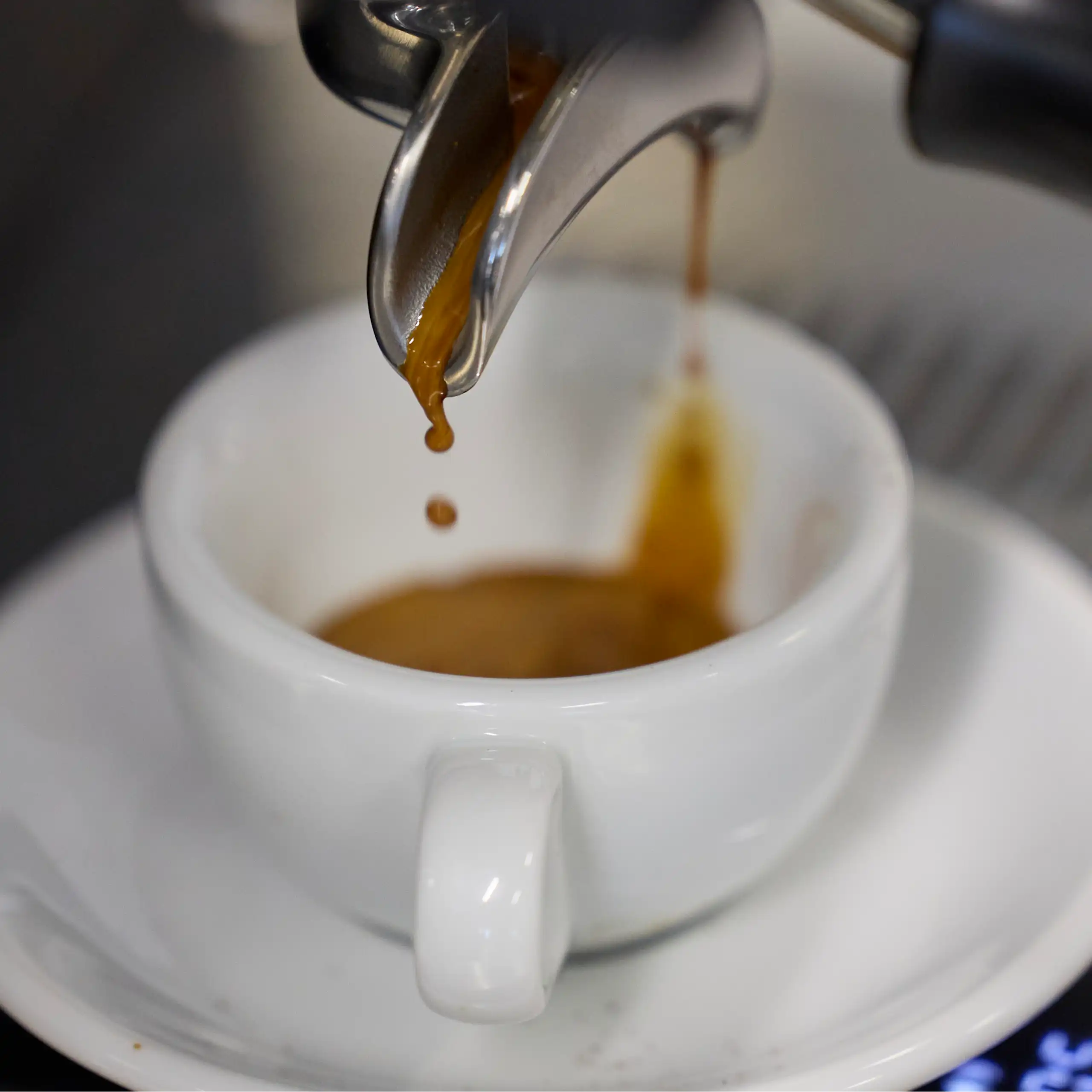 Espresso dripping from a coffee machine into a white cup.