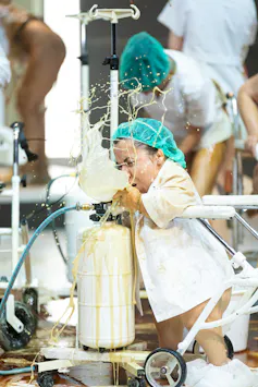 A performer in a white coat pretends to be vomiting onstage.