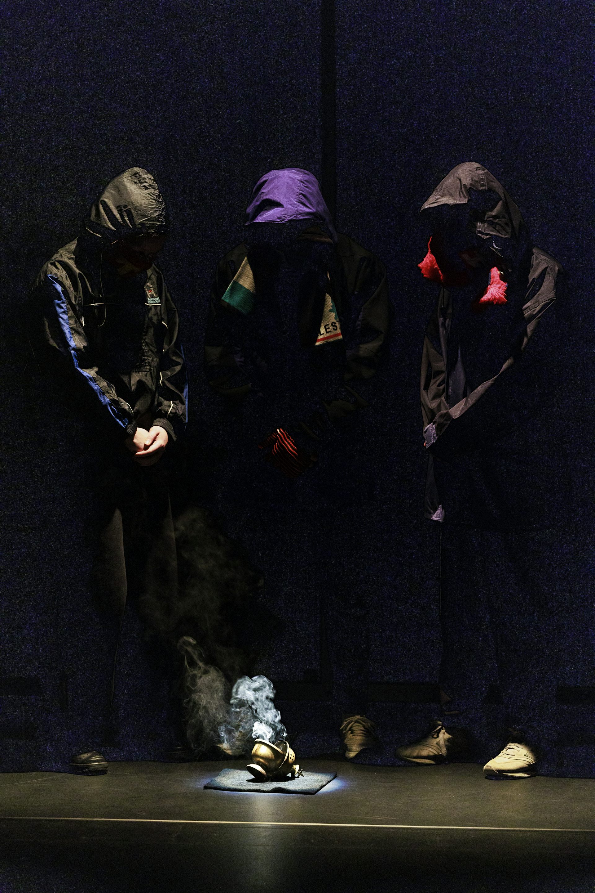 Three hooded figures stand around a smoking thurible.