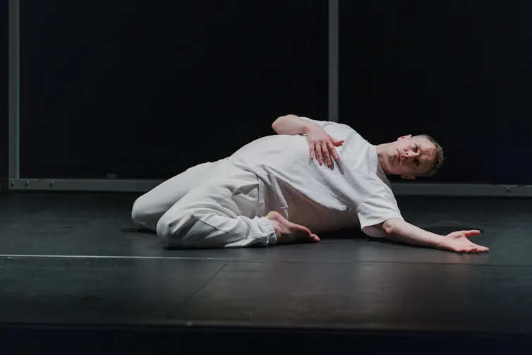 A dancer dressed in white is pictured on the ground mid-dance.