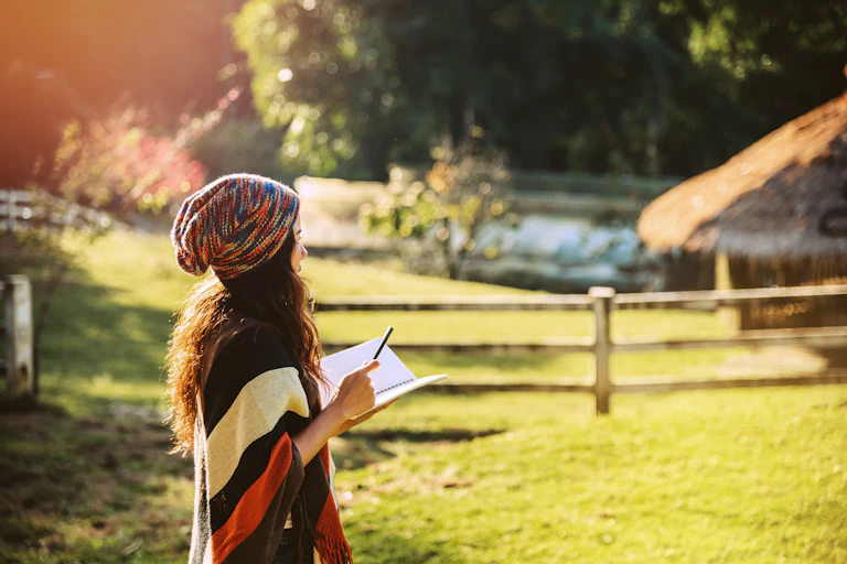 woman holding notebook and pen, standing in field