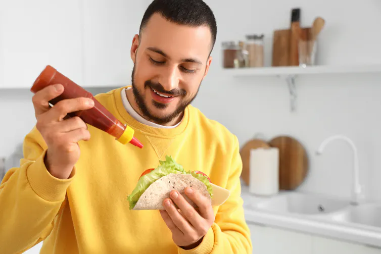 Young man eating tasty taco with hot sauce at home.