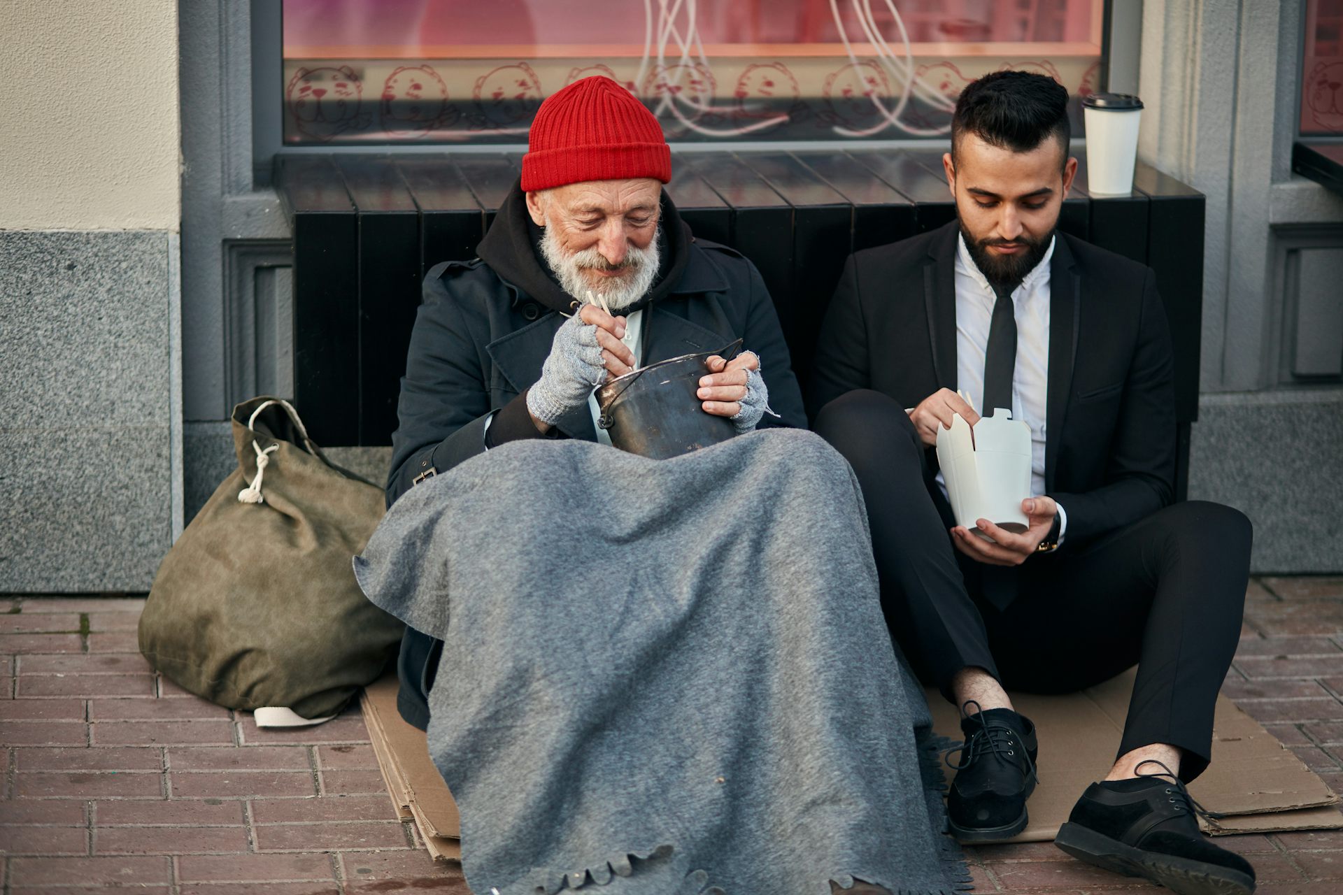 Stylish office worker and beggar male sit eating on street and speaking.