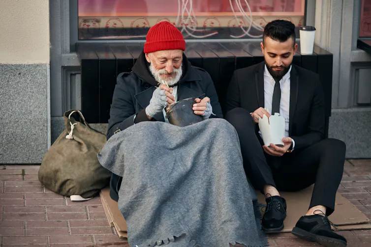 Stylish office worker and beggar male sit eating on street and speaking.