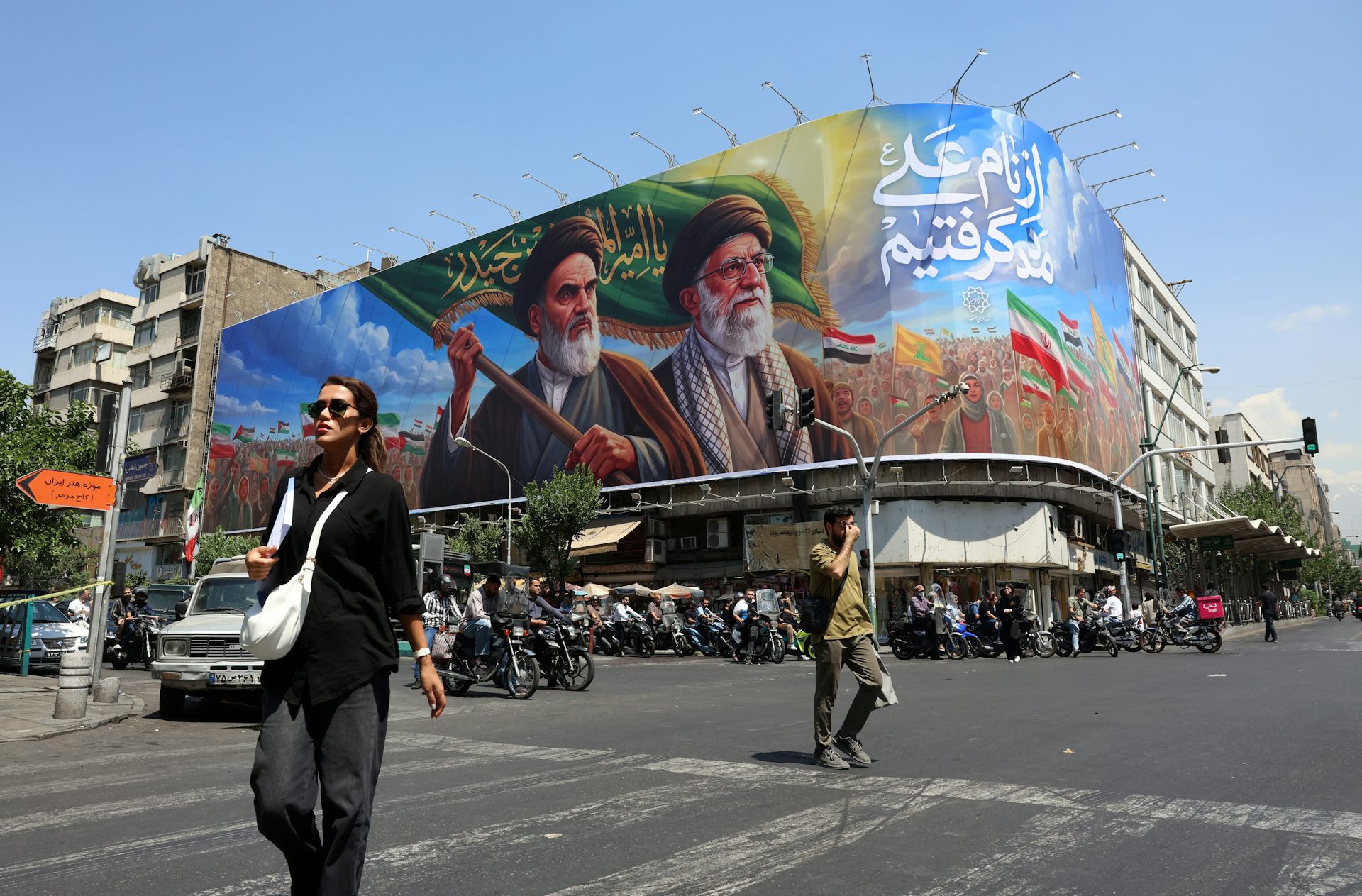 Iranians walk past a billboard featuring late Iranian supreme leaders, Ayatollah Ruhollah Khomeini and Ayatollah Ali Khamenei, on a street in Tehran.