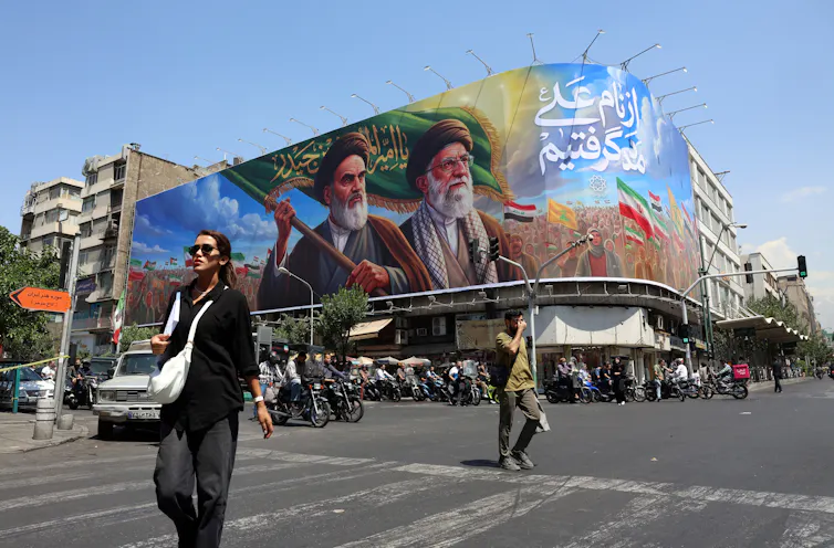 US and Iran’s trade of moves displays how some distance international relations has modified 1 Iranians walk past a billboard featuring late Iranian supreme leaders, Ayatollah Ruhollah Khomeini and Ayatollah Ali Khamenei, on a street in Tehran.