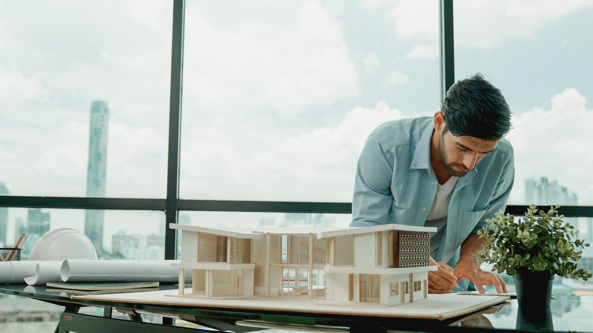 An architect making notes about his model building in front of huge glass windows.