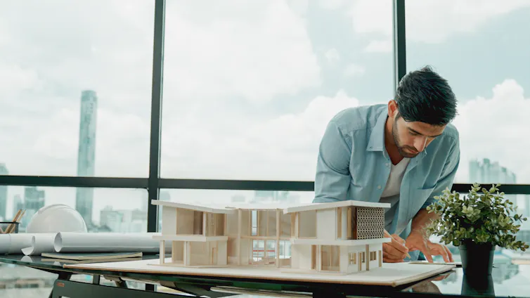 An architect making notes about his model building in front of huge glass windows.