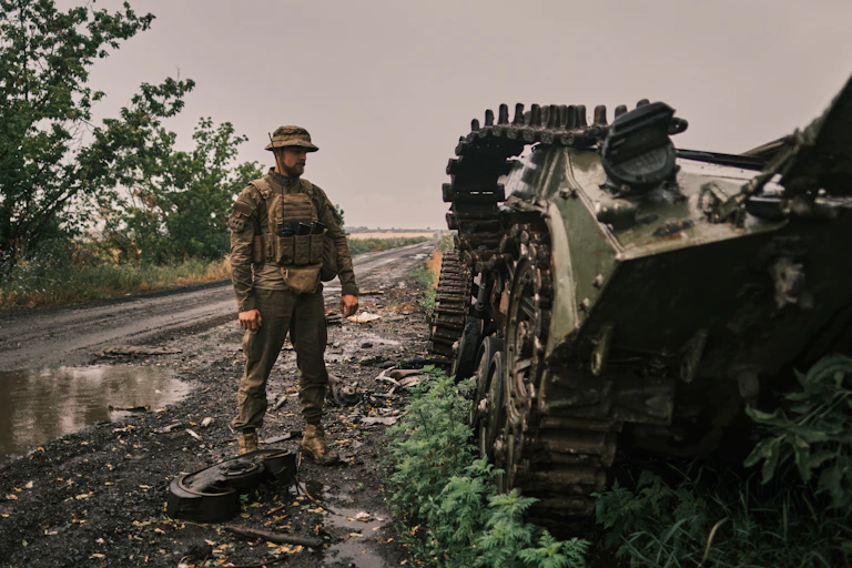 A Ukrainian soldier stands next to a damaged tank in Kharkiv Oblast.