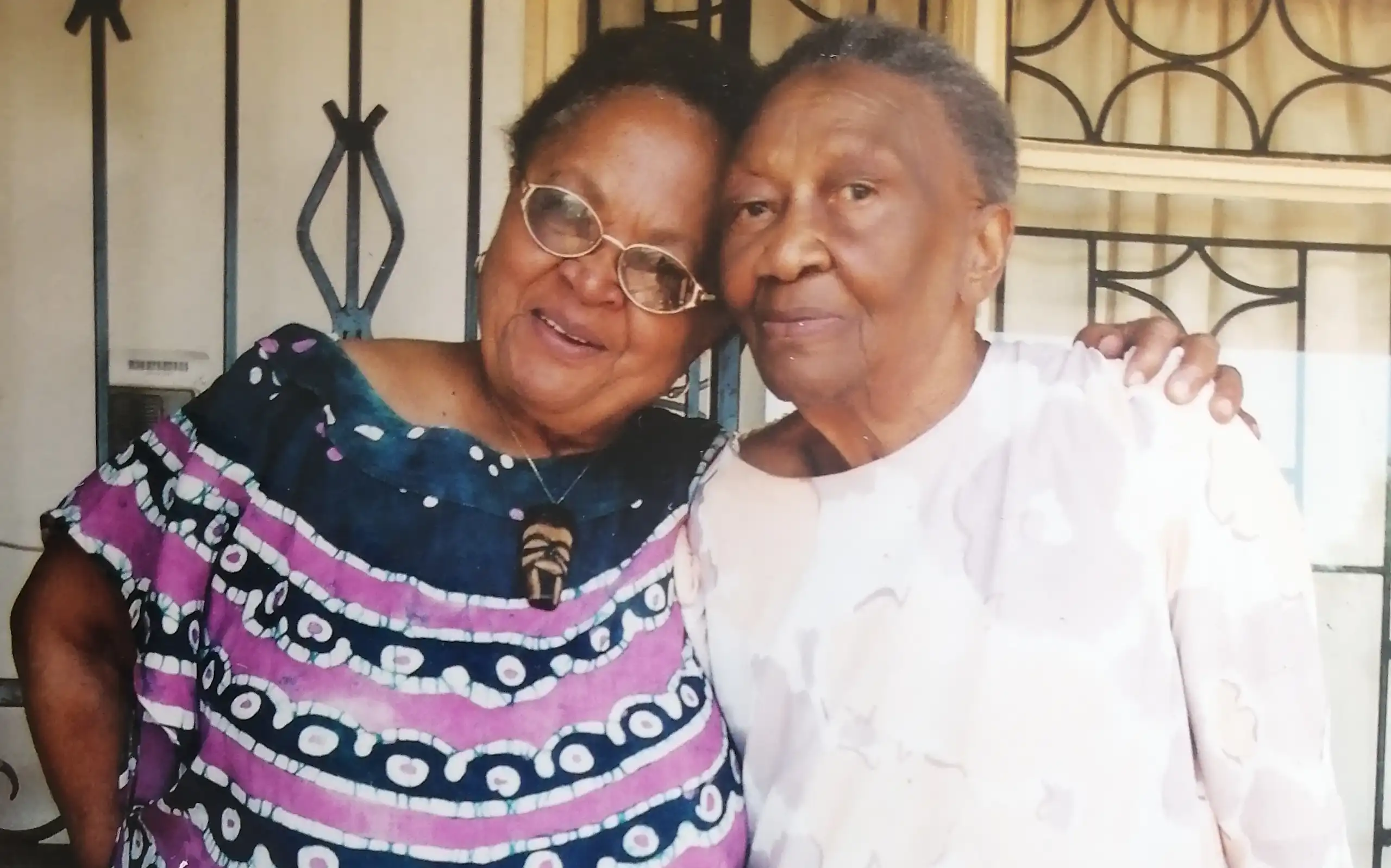 Two African women pose for a photo, heads touching, looking at the camera.