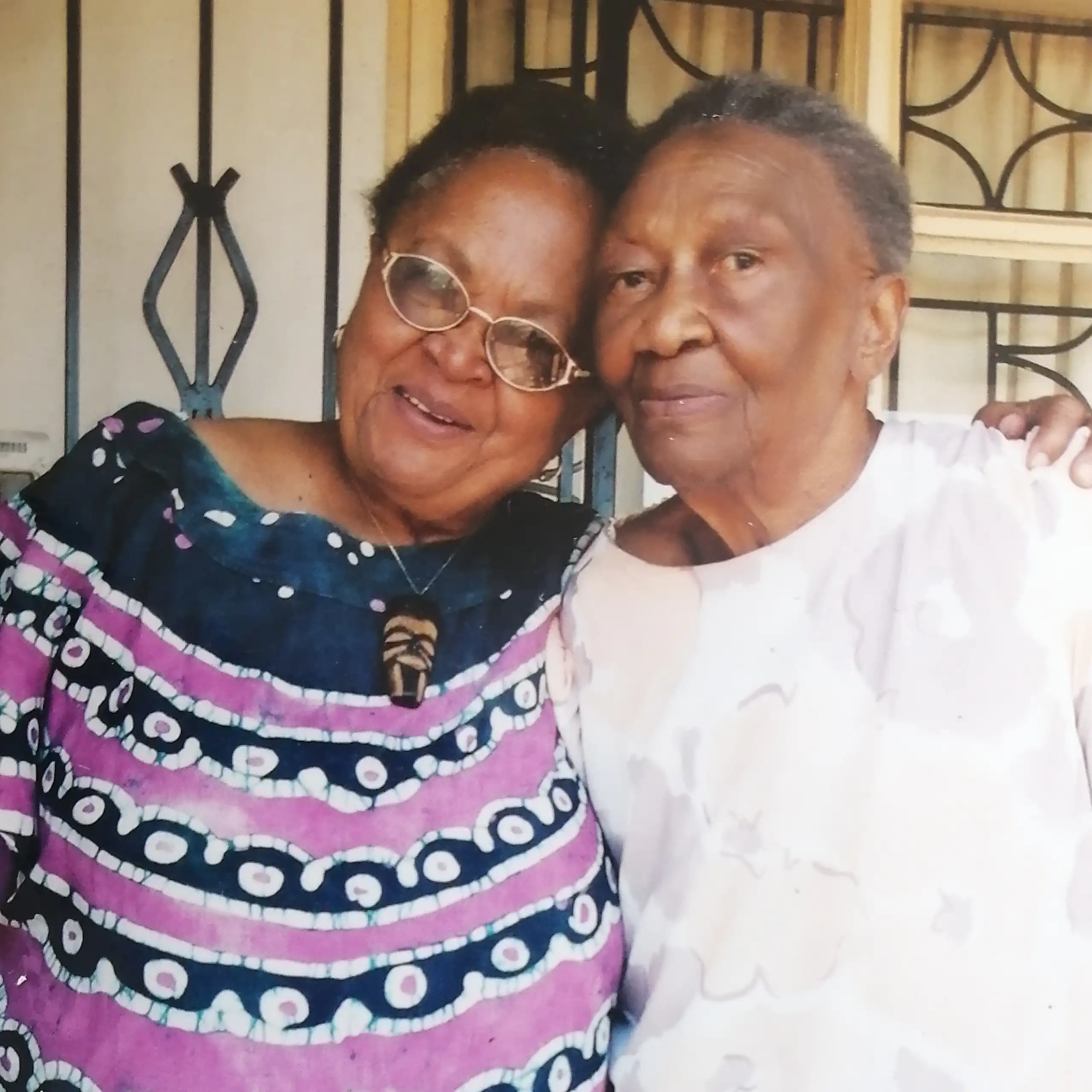 Two African women pose for a photo, heads touching, looking at the camera.