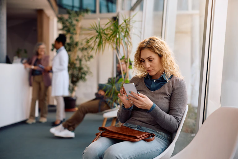 Une femme sur son smartphone, en train d'attendre un rendez-vous médical.