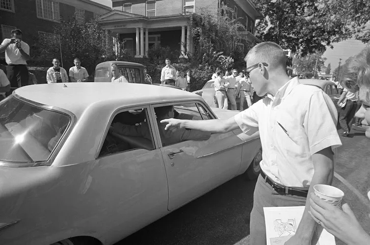 A white man points his finger at a Black man inside a car.