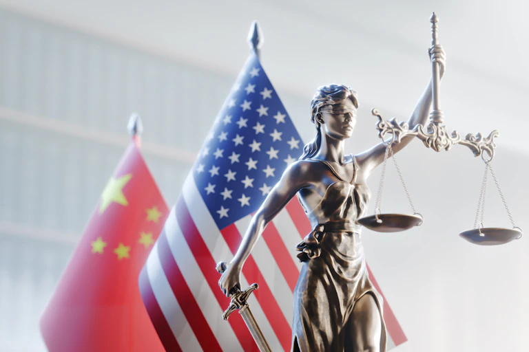 La Justice, aveugle, tenant sa balance à bout de bras avec, derrière elle, les drapeaux des États-Unis et de la Chine.