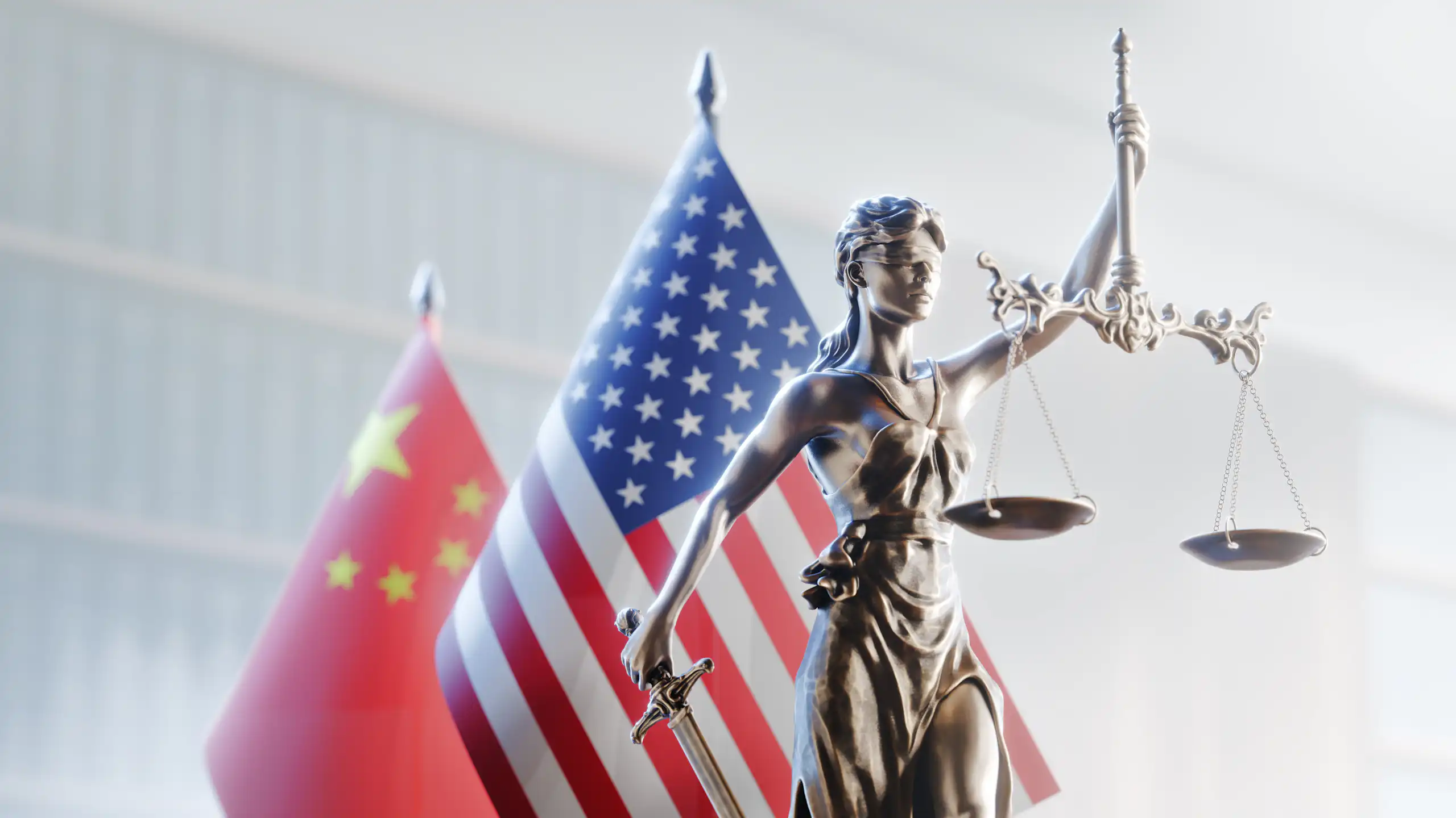 La Justice, aveugle, tenant sa balance à bout de bras avec, derrière elle, les drapeaux des États-Unis et de la Chine.