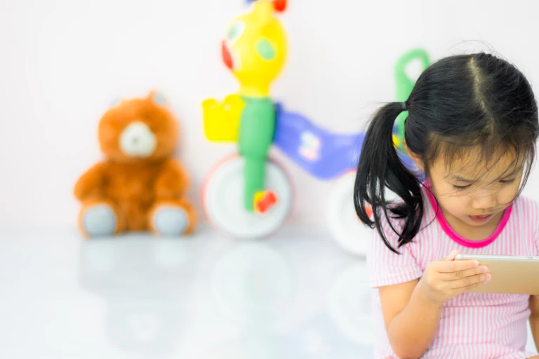 Girl playing on tablet with traditional toys behind her