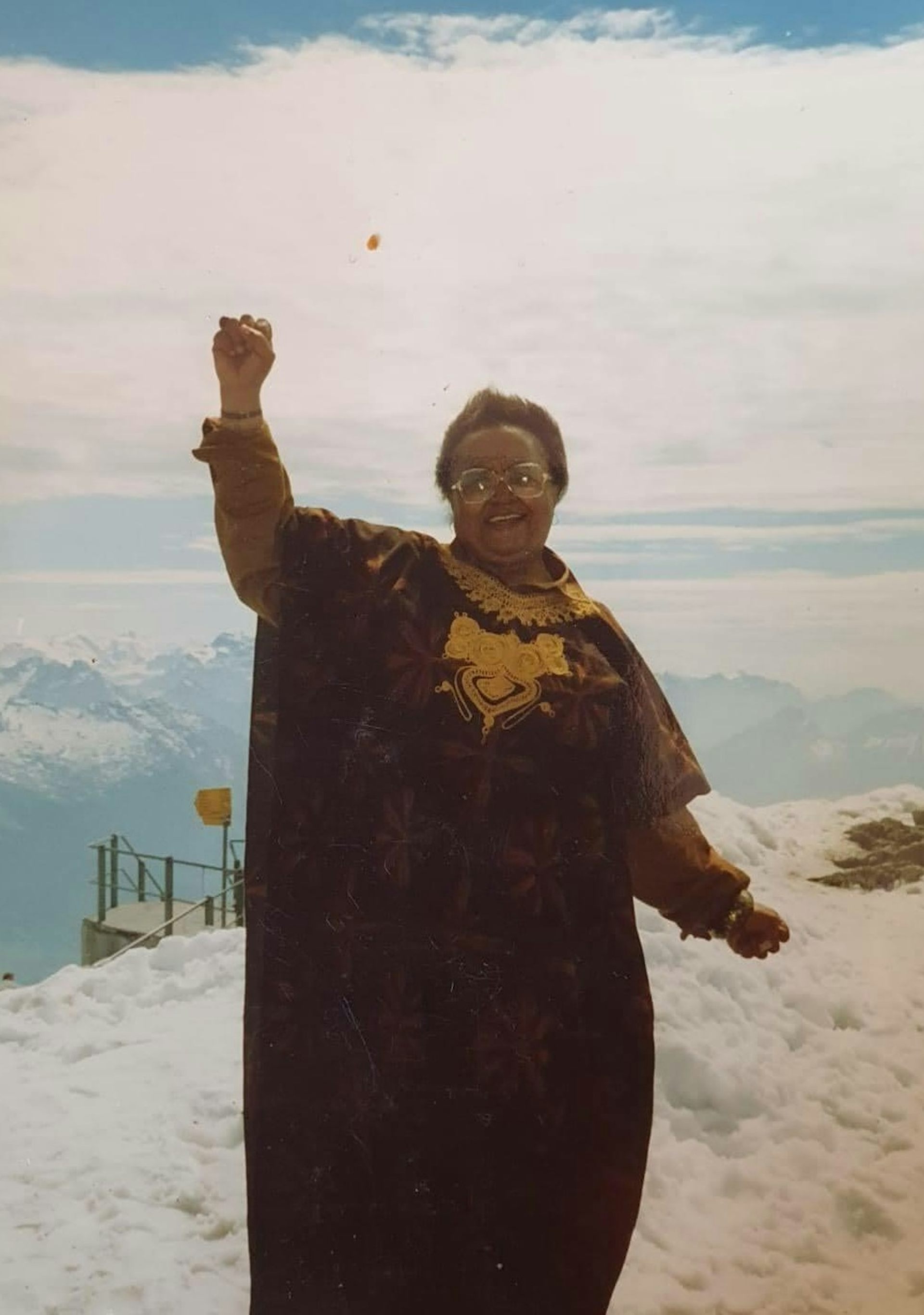 An African woman raises a fist at the top of a mountain.